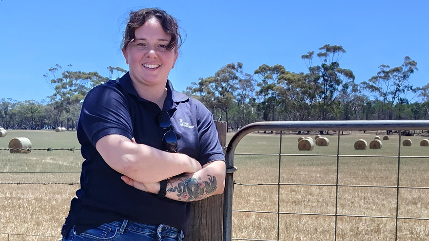 Hannah Griffiths from Dairy Australia leans against farm gate with arms crossed and a smile